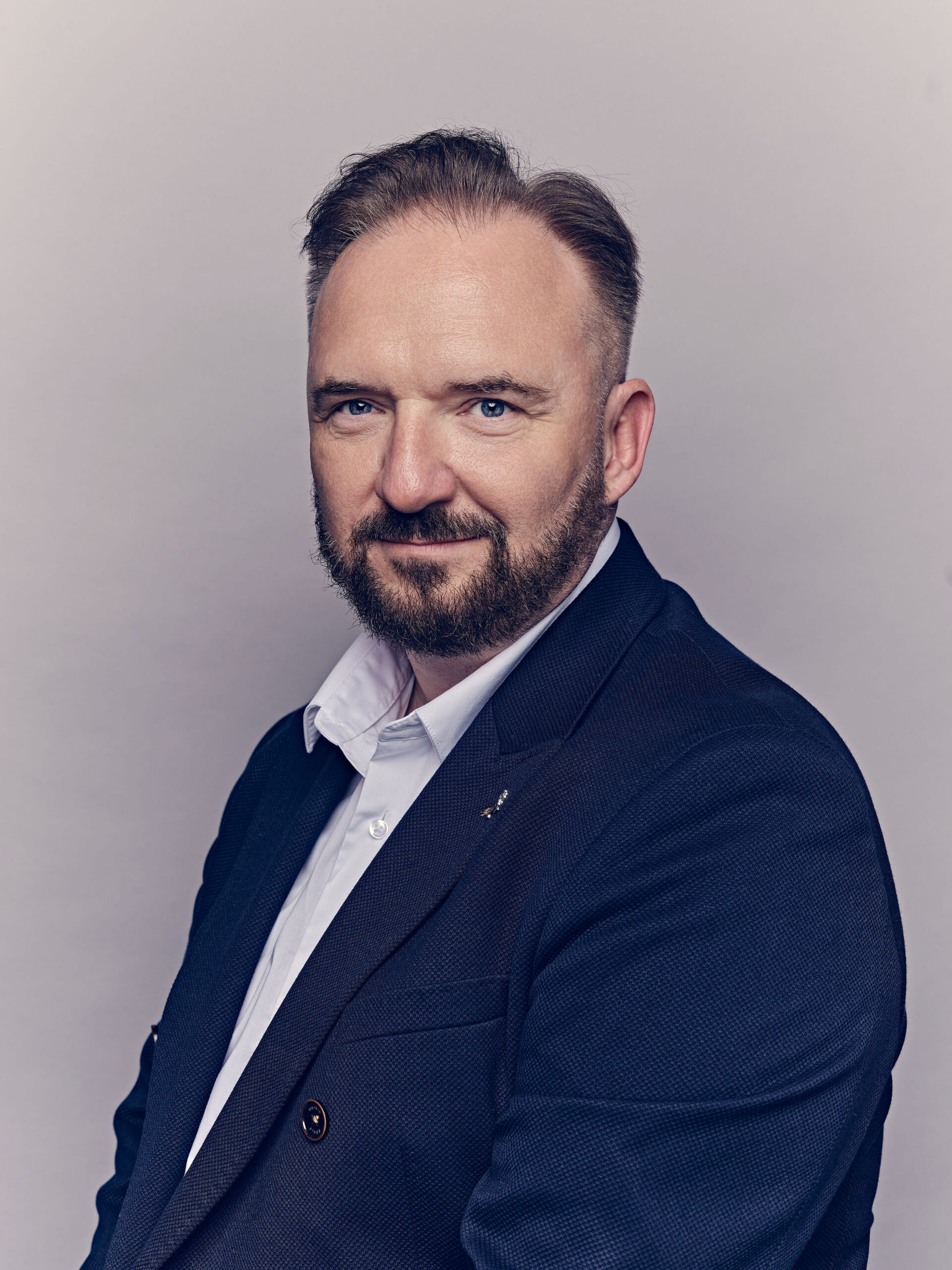Portrait of a man in a navy blazer and white shirt, facing slightly left, against a neutral backdrop.